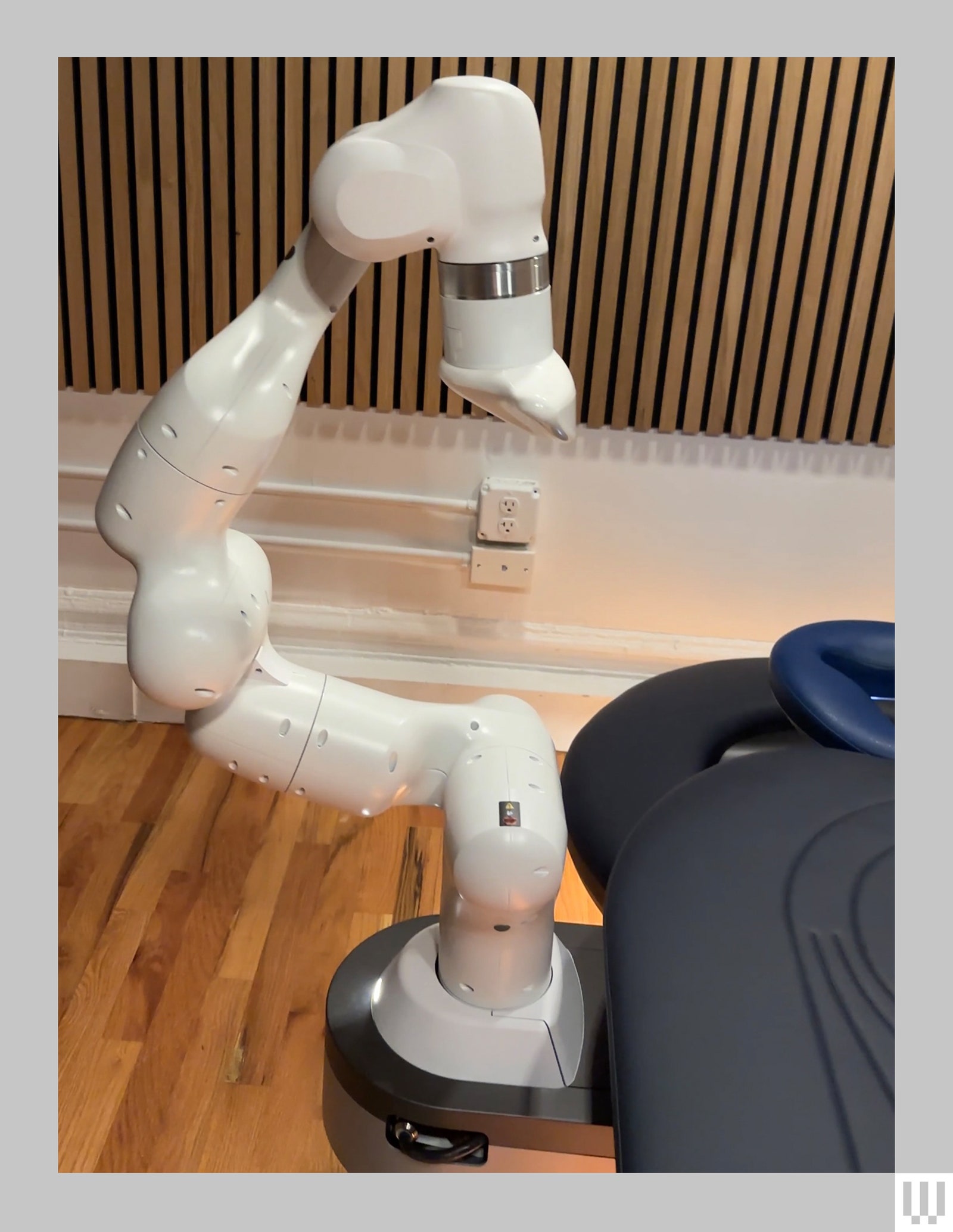 Side viw of white robotic arm attached to black padded massage table