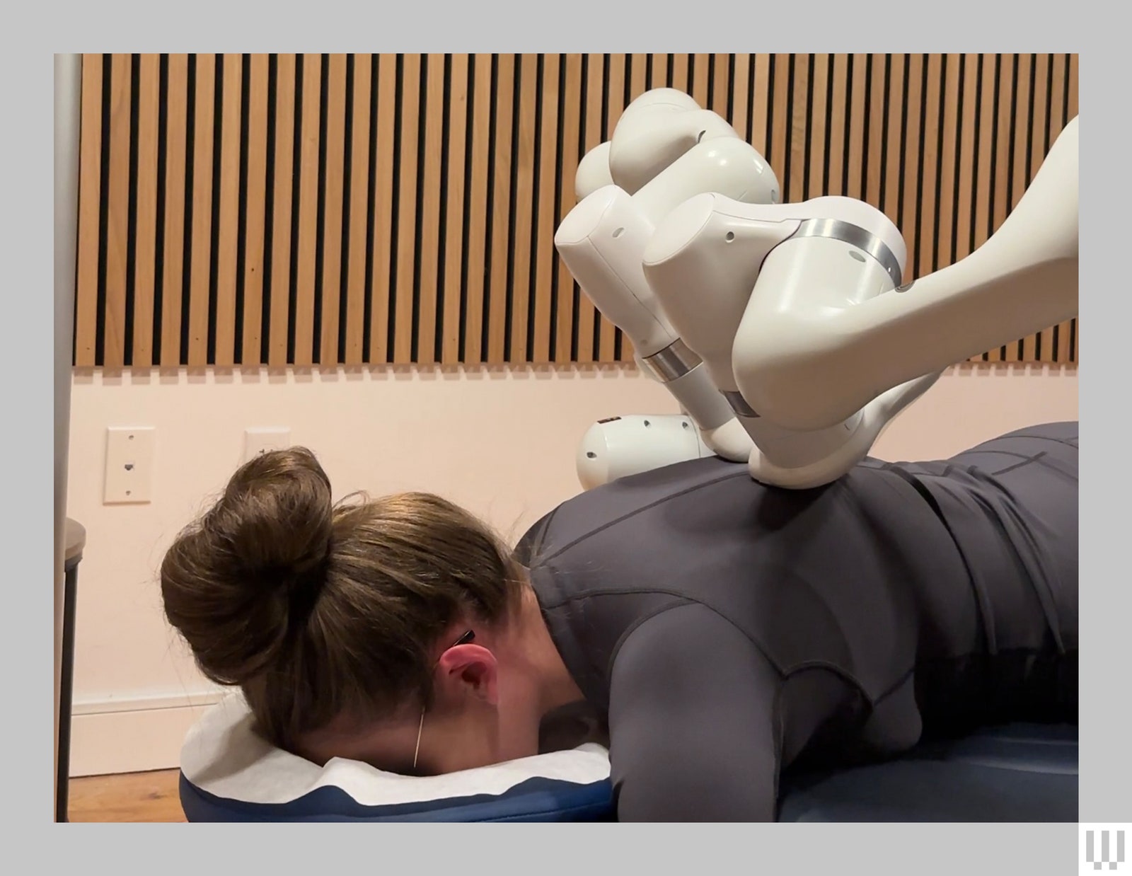 Person laying facedown on a massage table hair in a bun with a robotic arm conducting a massage on their upper back